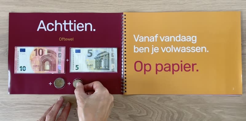 Een open boekje op tafel. Links staat Achttien, met een briefje van tien en vijf euro en twee munten erin; een hand legt de laatste munt. Rechts: Vanaf vandaag ben je volwassen. Op papier.